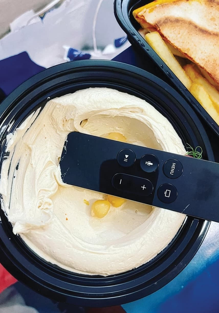 Television remote resting on a takeaway tub of hummus