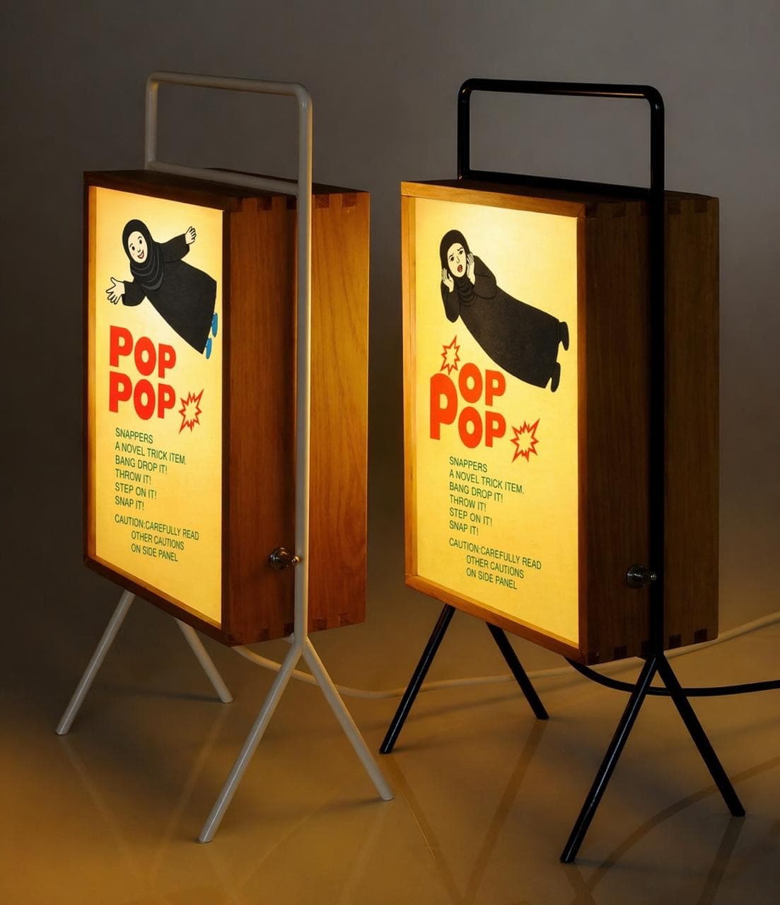 Two glowing POP POP lightboxes in wood cases on tripod legs, one white and one black